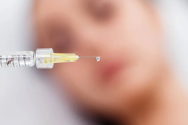 A drop of preparation hangs from the needle of the syringe against the face of the patient. Macro close upA drop of Botox hangs from the needle of the syringe against the face of the patient. Macro close up