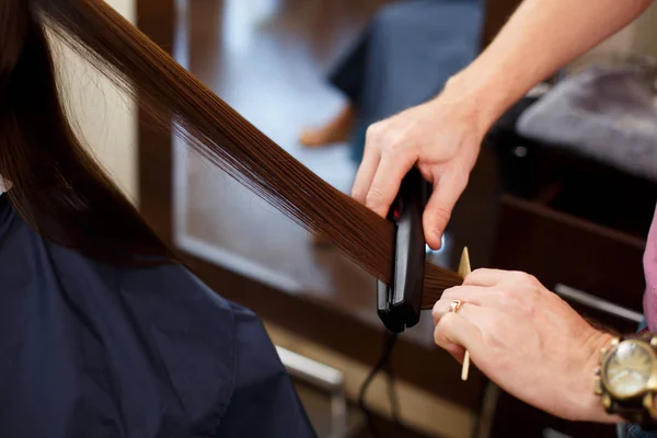 Man Stylist align the customer\'s hair with straightener
