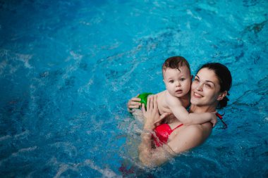Anneyle bebek havuzda yüzmeyi öğreniyor.