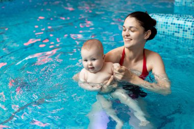Anneyle bebek havuzda yüzmeyi öğreniyor.