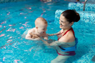 Anneyle bebek havuzda yüzmeyi öğreniyor.