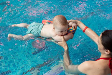 Anneyle bebek havuzda yüzmeyi öğreniyor.