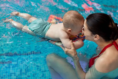 Anneyle bebek havuzda yüzmeyi öğreniyor.