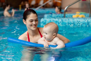 Anneyle bebek havuzda yüzmeyi öğreniyor.