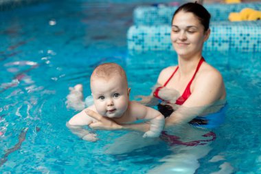 Anneyle bebek havuzda yüzmeyi öğreniyor.