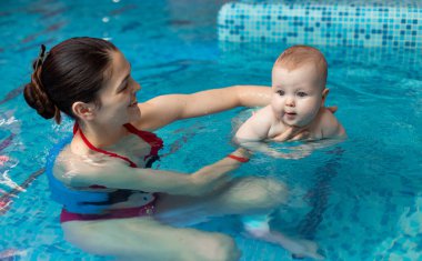 Anneyle bebek havuzda yüzmeyi öğreniyor.