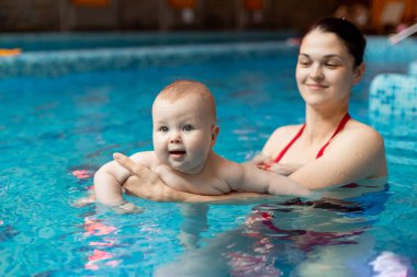 Anneyle bebek havuzda yüzmeyi öğreniyor.
