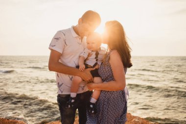Anne, baba ve oğul. Aile deniz kıyısındaki taşlı plajda geziniyor..