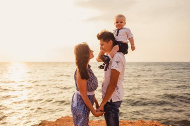 Anne, baba ve oğul. Aile deniz kıyısındaki taşlı plajda geziniyor..