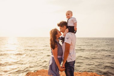 Anne, baba ve oğul. Aile deniz kıyısındaki taşlı plajda geziniyor..