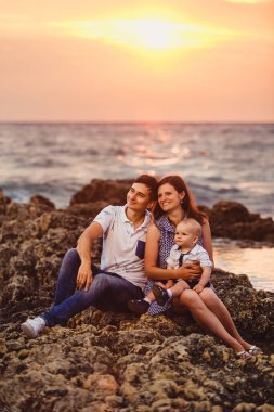 Anne, baba ve oğul. Aile deniz kıyısındaki taşlı plajda geziniyor..