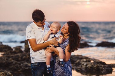 Anne, baba ve oğul. Aile deniz kıyısındaki taşlı plajda geziniyor..