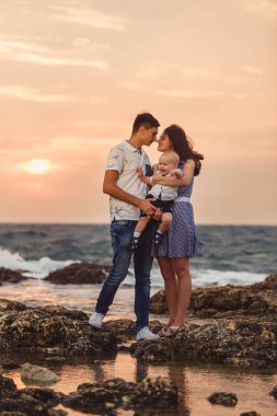 Anne, baba ve oğul. Aile deniz kıyısındaki taşlı plajda geziniyor..