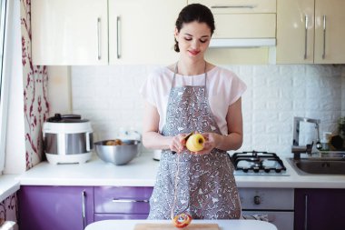 Mutfakta genç bir kadın elma soyar ve doğrar.