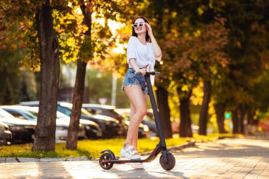 Yaz parkında scooter süren genç bir kadın.