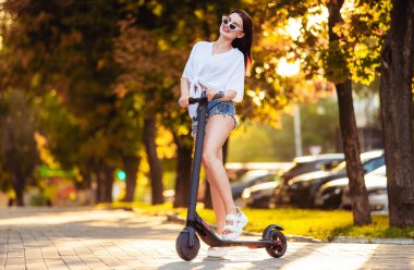 Yaz parkında scooter süren genç bir kadın.