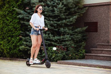 Yaz parkında scooter süren genç bir kadın.