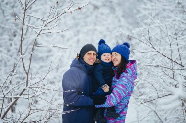 Anne baba ve küçük oğlu bir kış parkında kucaklaşıyorlar. Genç bir aile ormanda yürüyüşe çıktı.