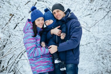 Anne baba ve küçük oğlu bir kış parkında kucaklaşıyorlar. Genç bir aile ormanda yürüyüşe çıktı.