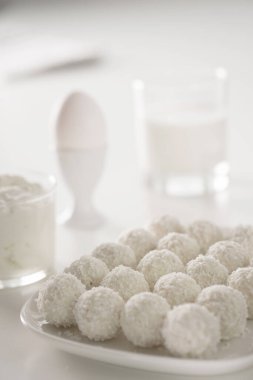 Kahvaltı - süt, yumurta, krem peynir ve raffaello hindistan cevizi şekerlemesi beyaz ahşap masada. Beyaz resim üzerine beyaz. Boş metin alanı olan arkaplan.