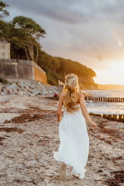 Gelin plajda. Beyaz elbiseli genç bir kadın plajda güneş ışığında koşuyor.