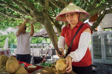 SANYA, CHINA - SEPTEMBER 13, 2015: Local woman cutting coconut clipart