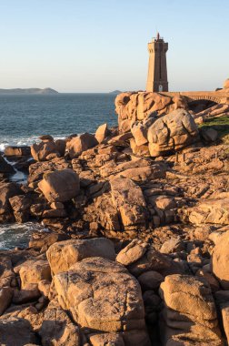 Deniz feneri ve Brittany Fransa kuzeybatı kesiminde alacakaranlıkta pembe granit kıyısında ikonik şekilli kayalar