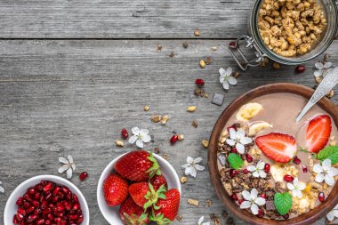 kakao veya çikolata ve muz protein güler yüzlü çiçek ve kahvaltı için rustik masa kaşık ile nar taneleri granola ile çilek, Bovling. üstten görünüm. sağlıklı kahvaltı