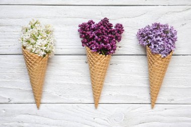 Beyaz ahşap arka plan üzerinde renkli eflatun çiçekli dondurma külah. üstten görünüm. düz lay