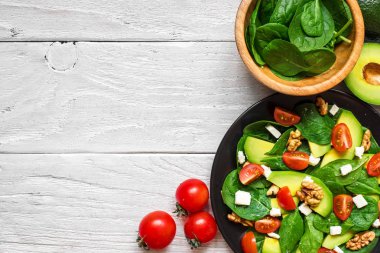 Taze salata avokado, ıspanak, domates kiraz, beyaz peynir ve ceviz Beyaz ahşap masa üzerinde bir tabak içinde. üstten görünüm kopya alanı ile. sağlıklı gıda