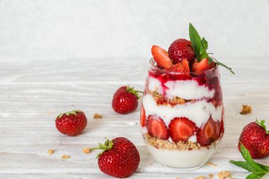 çilekli yoğurt granola, nane ve beyaz tahta masada bir bardak taze çilek parfe. sağlıklı kahvaltı