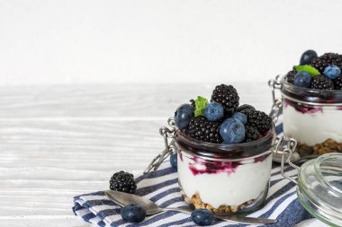 Yunan yoğurtlu taze yaban mersini, böğürtlen, granola, reçel ve kavanoz Mutfak havlu üzerinde beyaz ahşap masa üzerinde bir kaşıkla nane. sağlıklı kahvaltı. yukarıdan görüntülemek