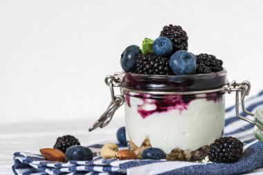 sağlıklı berry yoğurtlu taze yaban mersini, böğürtlen, granola, fındık ve nane bir kavanoz Mutfak havlu üzerinde beyaz ahşap masa üzerinde. sağlıklı kahvaltı. kopya alanı ile yakın çekim