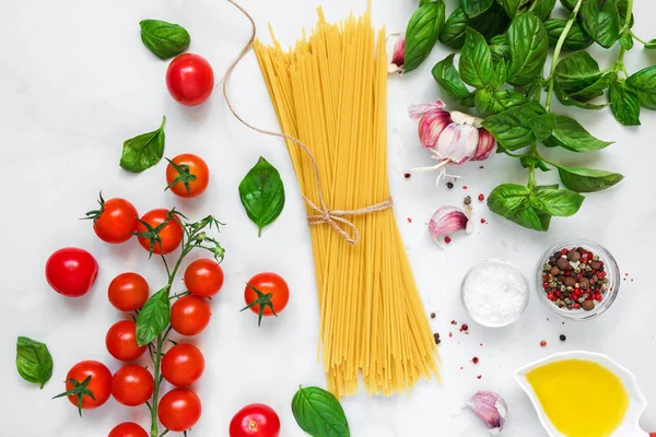 pişmemiş makarna spagetti domates, sarımsak ve beyaz mermer zemin üzerine fesleğen. pişirme kavramı. üstten görünüm. düz lay