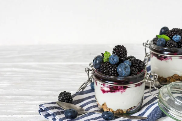 Yunan yoğurtlu taze yaban mersini, böğürtlen, granola, reçel ve kavanoz Mutfak havlu üzerinde beyaz ahşap masa üzerinde bir kaşıkla nane. sağlıklı kahvaltı. yukarıdan görüntülemek