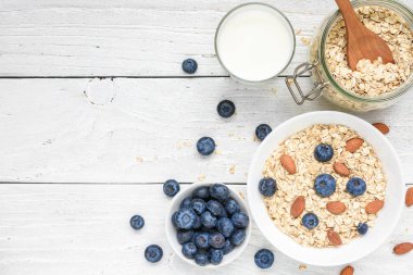Taze yaban mersini, süt ve beyaz ahşap bir masa üzerinde fındık ile yulaf gevreği. sağlıklı kahvaltı. kopya alanı ile üstten görünüm