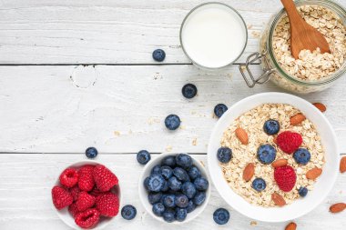 Taze meyveleri ve beyaz ahşap bir masa üzerinde fındık ile yulaf gevreği. sağlıklı kahvaltı. kopya alanı ile üstten görünüm