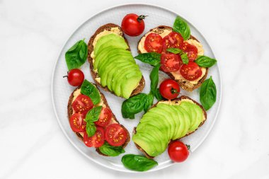avokado, domates, humus ve fesleğen beyaz mermer masa üzerinde sağlıklı kahvaltı tost. vegan gıda. üstten görünüm