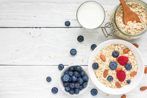 Healthy breakfast ingredients. homemade oats with raspberries and blueberries, milk and nuts for muesli on white wooden background. top view with copy space