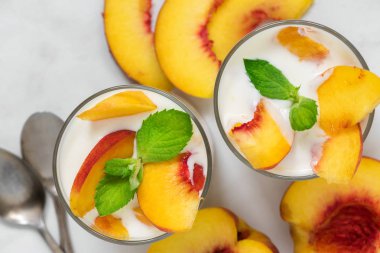 sağlıklı meyve yoğurtlu Taze şeftali, kaşık ve nane beyaz mermer masada iki kadeh. sağlıklı kahvaltı. üstten görünüm