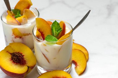 sağlıklı meyve yoğurtlu Taze şeftali, kaşık ve nane beyaz mermer masada iki kadeh. sağlıklı kahvaltı. yakın çekim