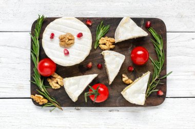 camembert peyniri domates kiraz, nar taneleri, ceviz ve biberiye ahşap kesme tahtası üzerinde. üstten görünüm