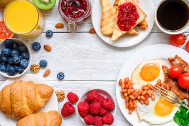 İngiliz kahvaltısı - kızarmış yumurta, fasulye, domates, kahve, pastırma ve portakal suyu, taze meyve ve çilek ile tost. Kopya alanı ile üstten görünüm