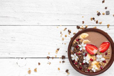 kakao muz protein güler yüzlü kase çikolata granola, çilek ve nar tohumları ile çiçeklerle süslenmiş. üstten görünüm kopya alanı ile. sağlıklı kahvaltı
