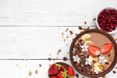 Çikolata muz protein güler yüzlü kase çiçeklerle tepesinde granola, çilek ve nar tohumları ile. üstten görünüm kopya alanı ile. sağlıklı kahvaltı