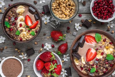 Çikolata muz protein smoothie granola ile çilek, nar ve çikolata barları rustik ahşap masa günü kahvaltıda servis kase. üstten görünüm. sağlıklı kahvaltı