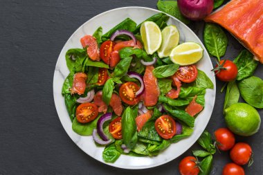 Ispanak, cherry domates, kırmızı soğan ve fesleğen taş koyu arka plan üzerinde mermer plaka ile somon salata. sağlıklı gıda kavramı. üstten görünüm
