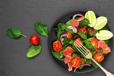 taze salata somon, ıspanak, domates, kırmızı soğan ve fesleğen ile çatal siyah arduvaz arka plan üzerinde siyah plaka ile. sağlıklı gıda kavramı. üstten görünüm