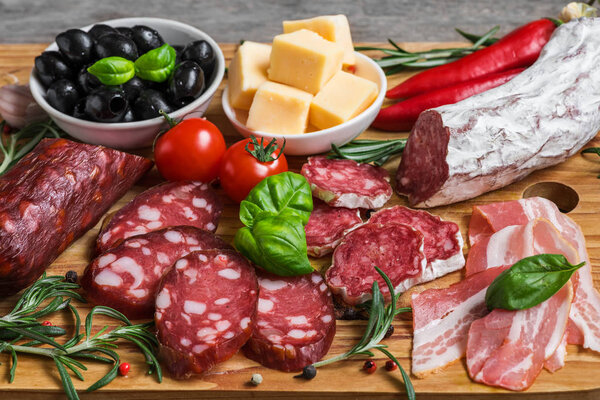 Salami, sliced bacon, sausage, cheese, olives, tomatoes and herbs. Meat antipasto platter on wooden table. close up