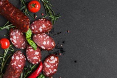 Salam baharat, domates ve biberiye ile siyah arduvaz arka plan üzerine dilimlenmiş. kopya alanı ile üstten görünüm